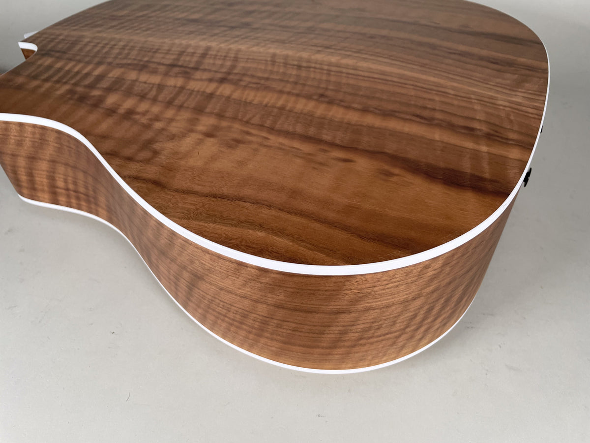 Close-up of the acoustic guitar's lower bout, showing the natural wood grain on the back and side, with white binding.