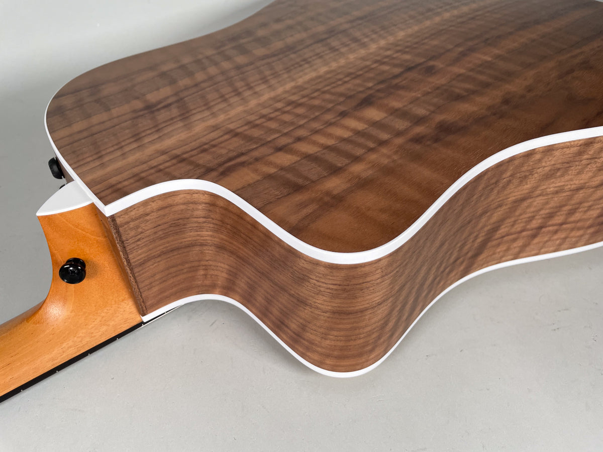 Upper bout of a natural finish acoustic guitar, showing the dark brown wood grain, white binding, and light brown neck heel.