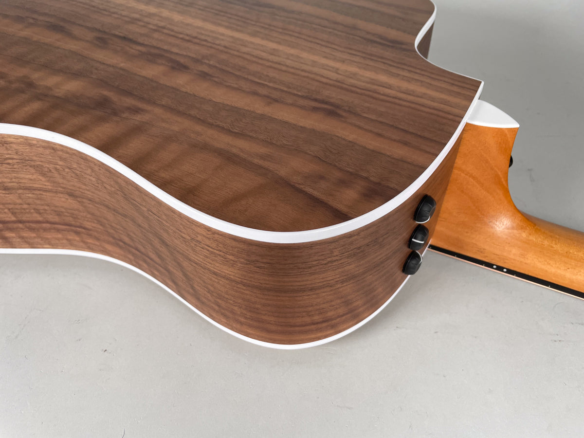 Close-up of a guitar's lower bout and cutaway, showing the dark wood grain, white binding, three black control knobs, and light wood neck.