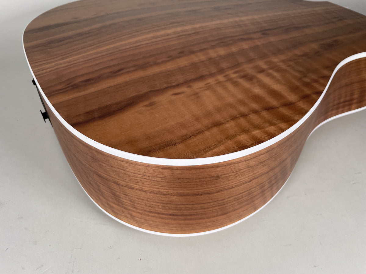 The lower bout and side of the natural finish acoustic guitar, showing the wood grain and white binding.