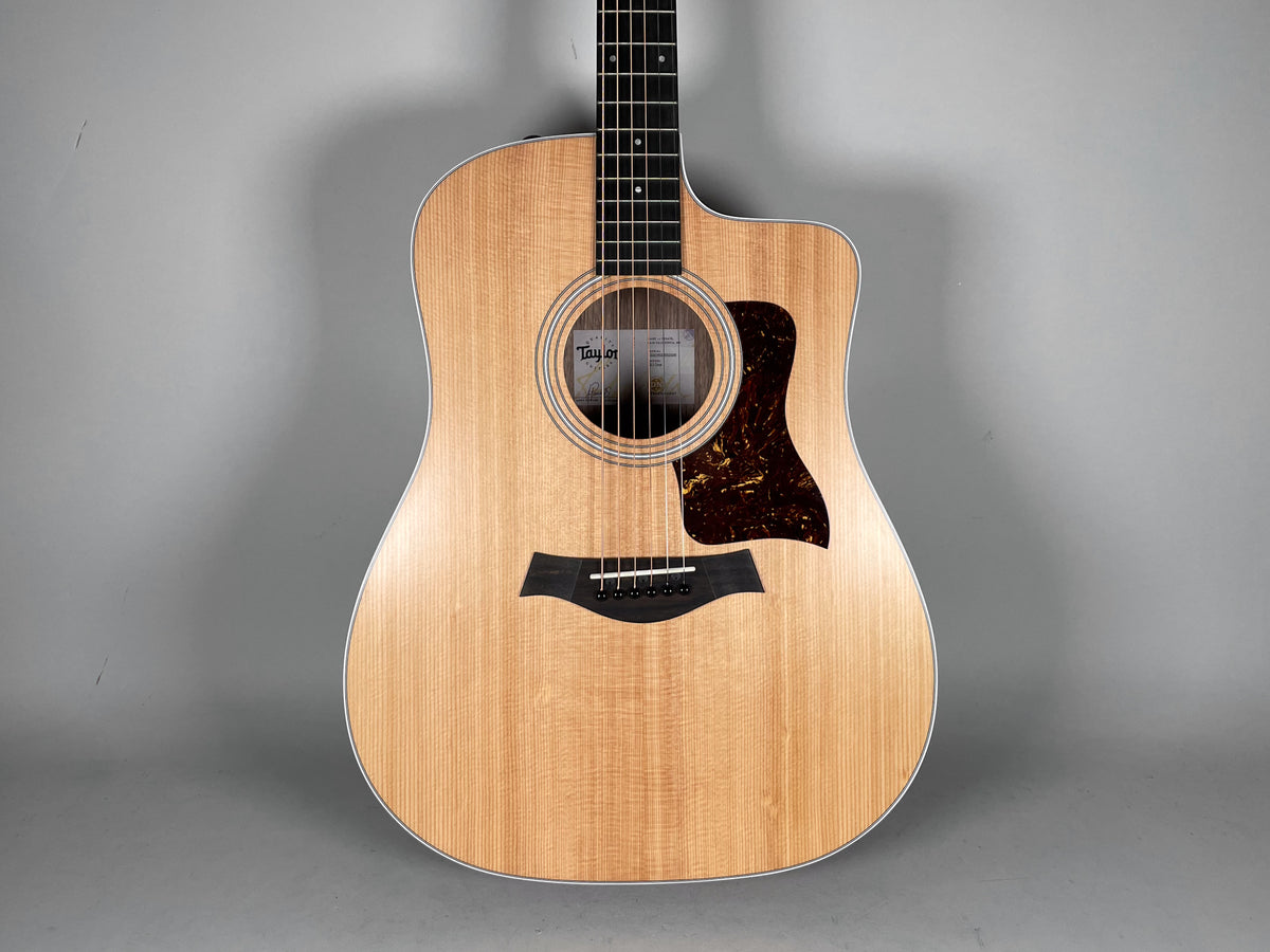 Natural finish acoustic guitar, full front view, showing light wood grain, dark tortoise pickguard, and black bridge.
