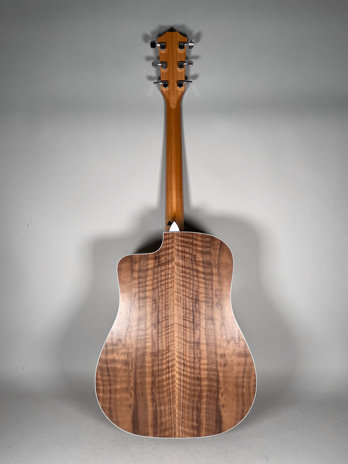 The acoustic guitar is viewed from the back, showing the natural wood grain of the body and neck, with chrome tuners on the headstock.