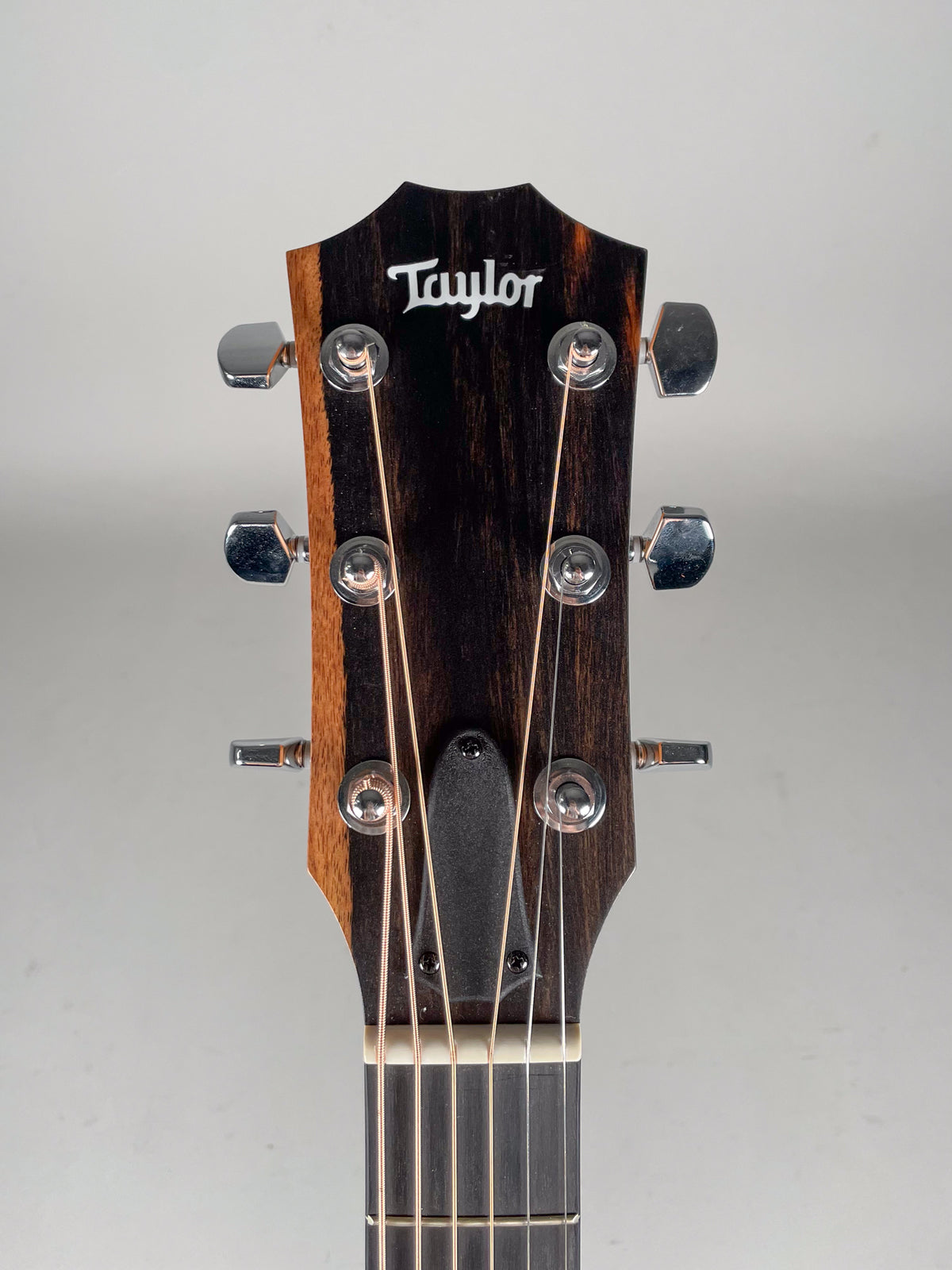 Close-up of the guitar's headstock, featuring a dark wood grain, chrome tuners, and a black truss rod cover.