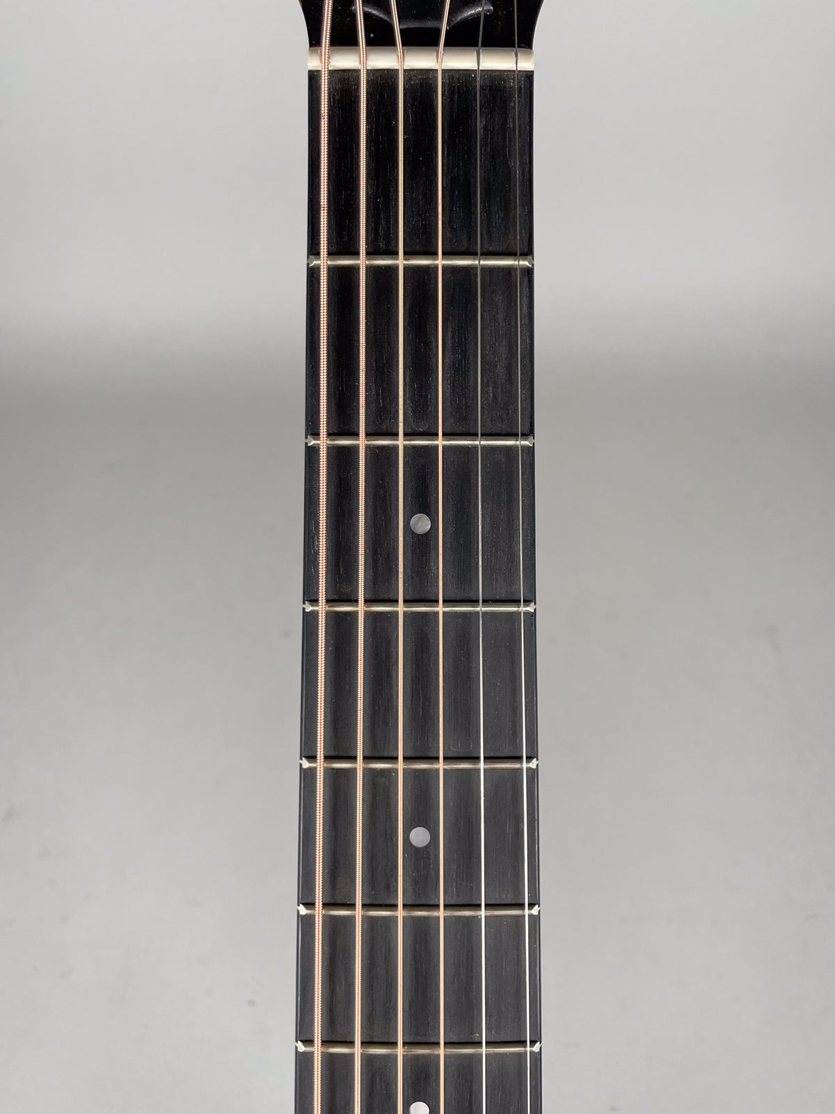 Close-up of the dark fretboard with light strings, showing five frets and two circular fret markers.