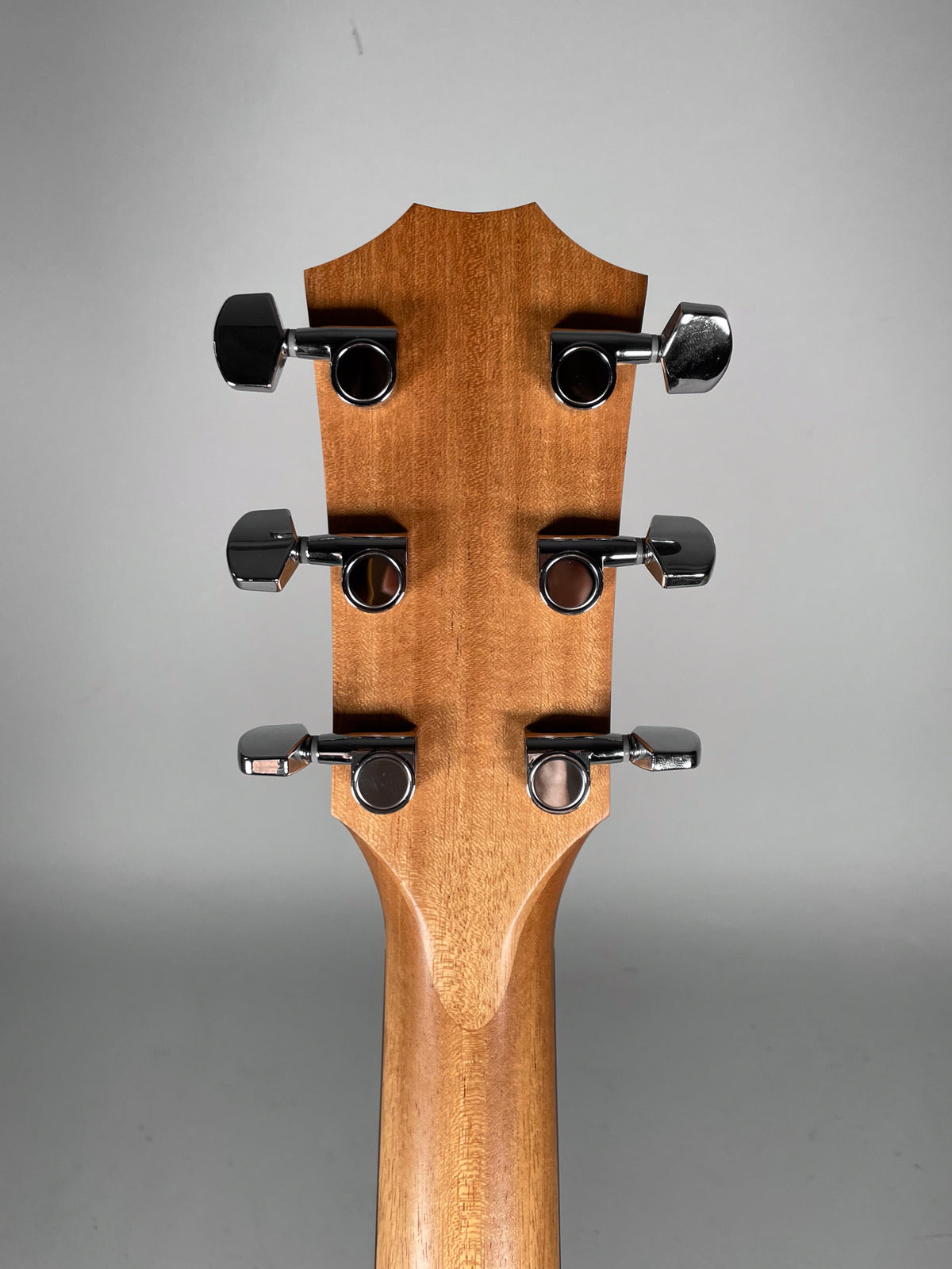 The back of the guitar's headstock and upper neck, showing six chrome tuning machines on the light brown, natural wood finish.