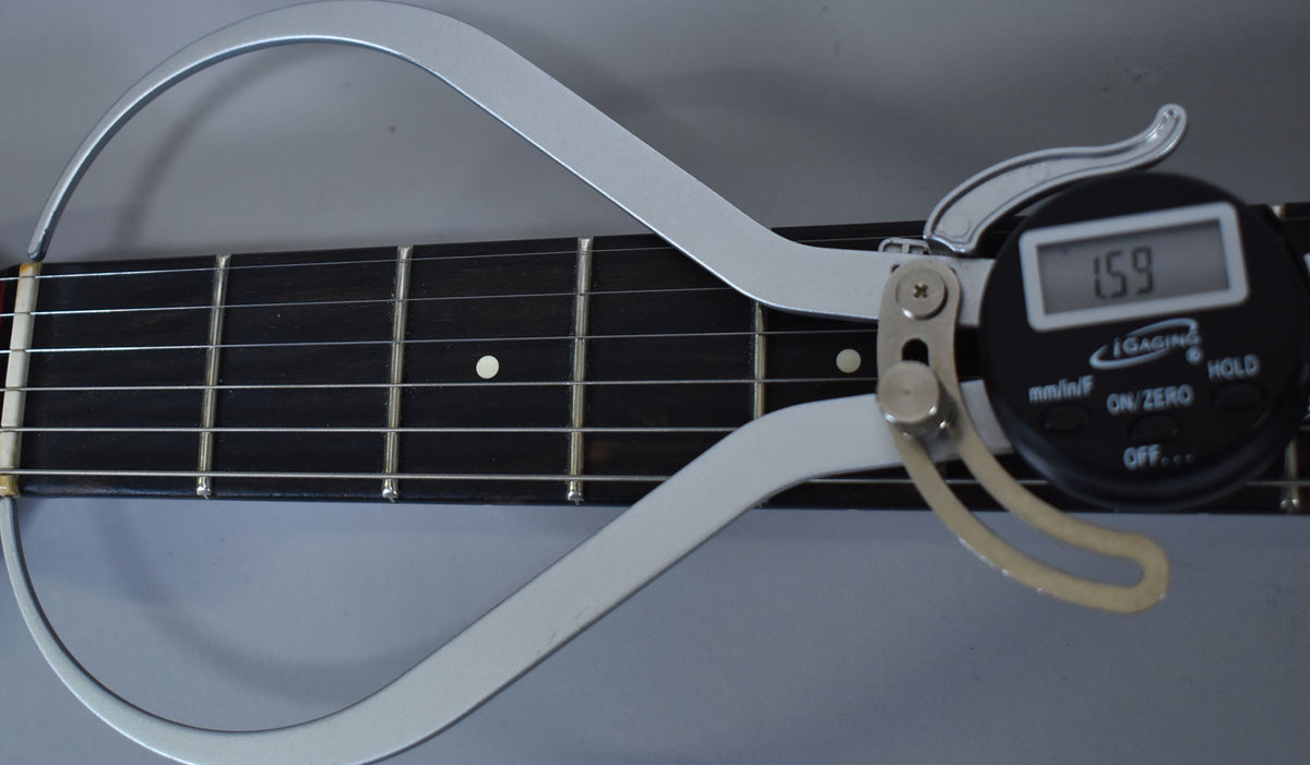 A digital caliper measures the fretboard and strings of the Racing Red guitar, displaying "1.59" on its screen.