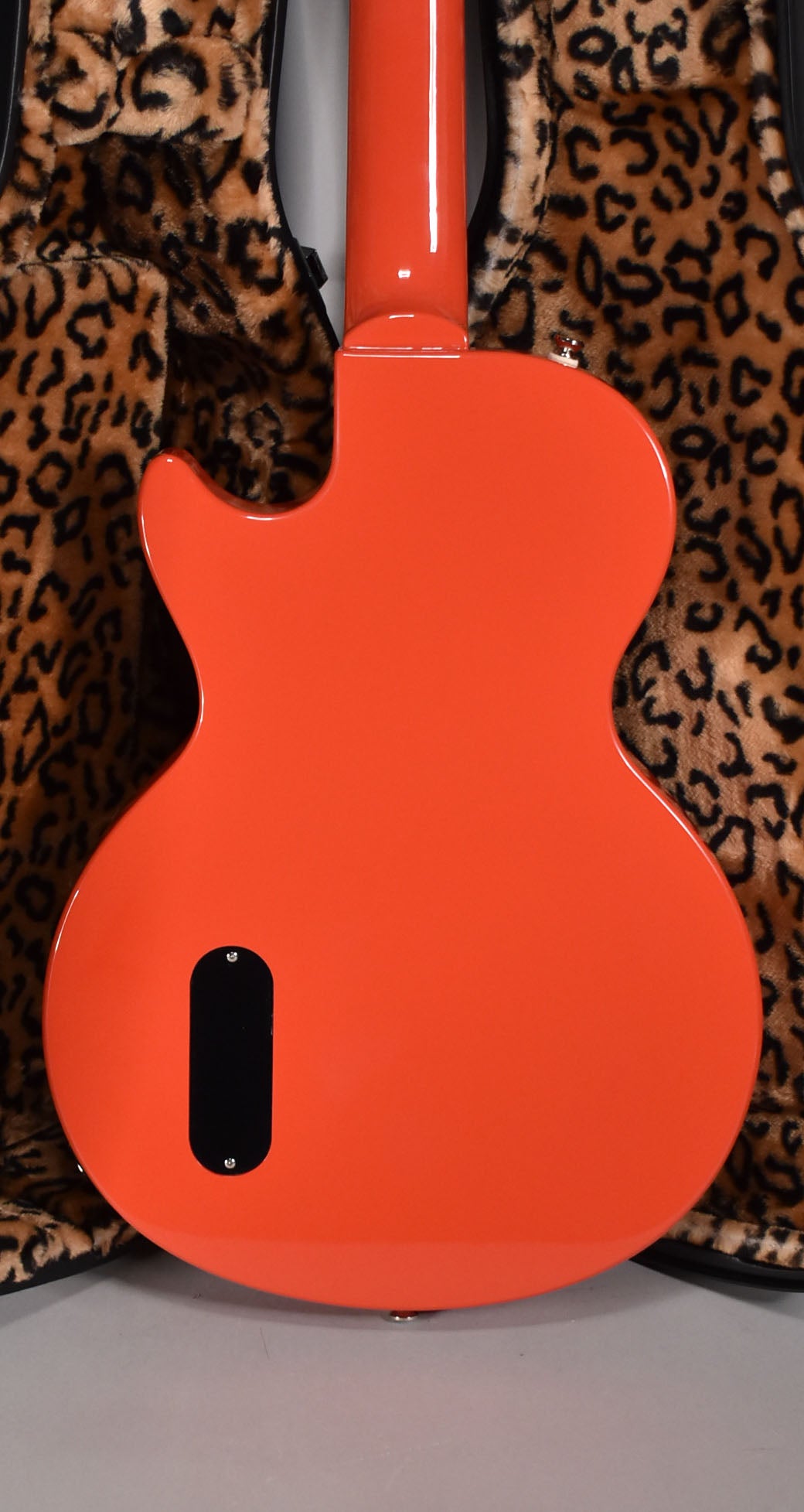 The guitar's glossy radiant red back, with a black control cavity cover, rests on a leopard print case lining.