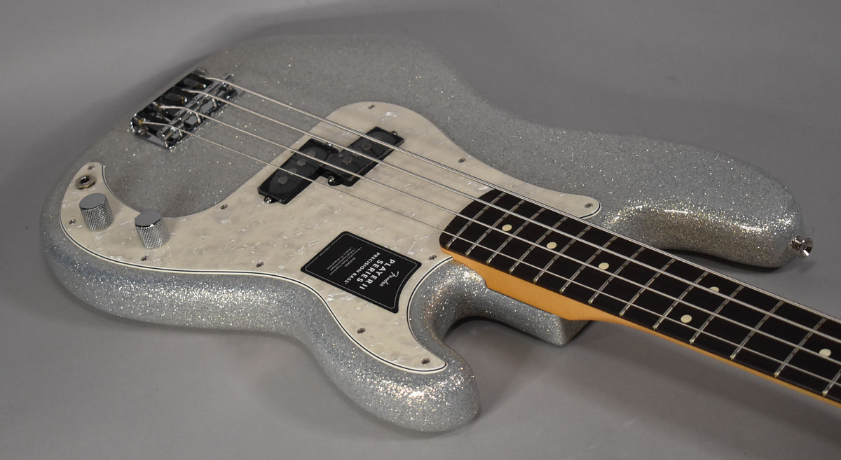 Silver sparkle bass, angled from above, showing the body, pearloid pickguard, two chrome knobs, and rosewood fretboard.