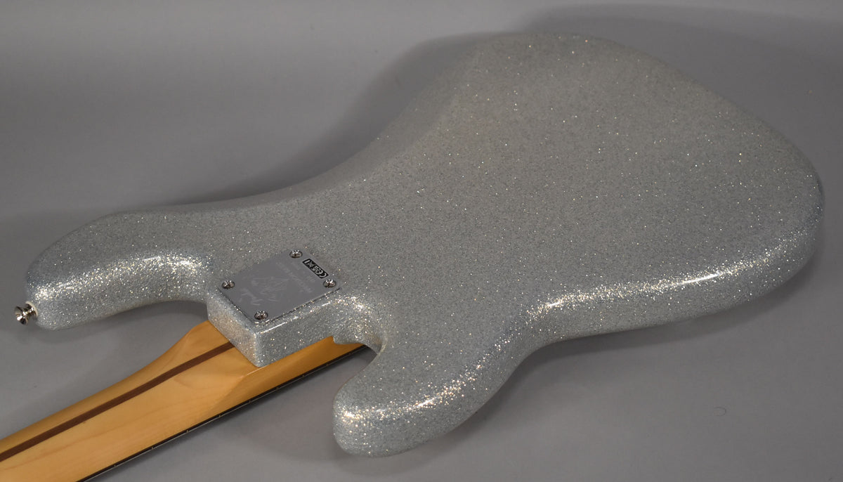 The bass's silver sparkle body is viewed from the back, showing the chrome neck plate and a light wood neck with a dark stripe.