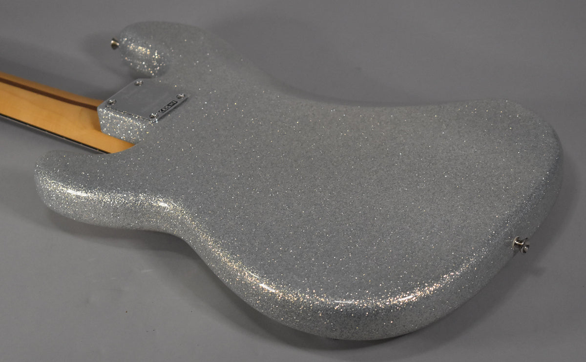 The back of a silver sparkle bass body, angled from the neck joint to the lower bout, with a chrome neck plate and strap button.