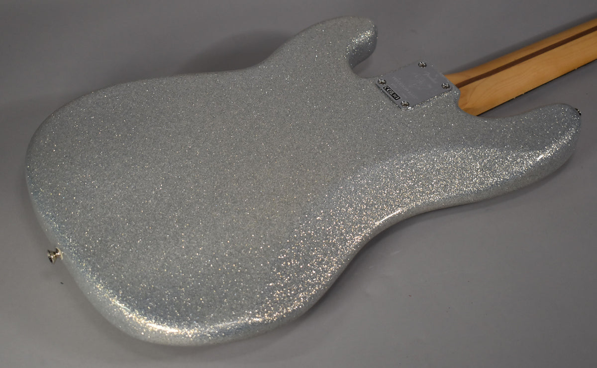 The back of a silver sparkle bass body is angled from the lower left, with a light wood neck extending to the upper right.