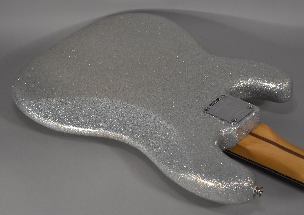 The back of a silver sparkle bass body, angled from the lower bout to the neck plate, showing a chrome strap button.