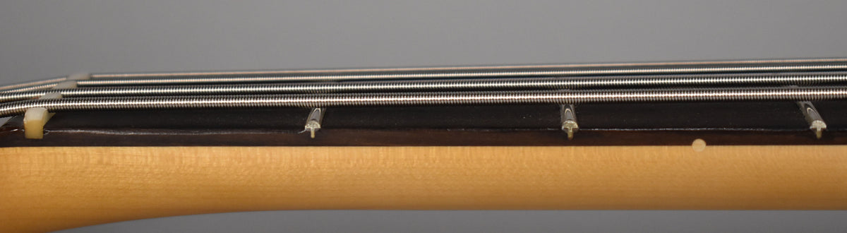 Close-up of the bass neck from the side, showing the light maple neck, dark fretboard, and four silver strings over a white nut.