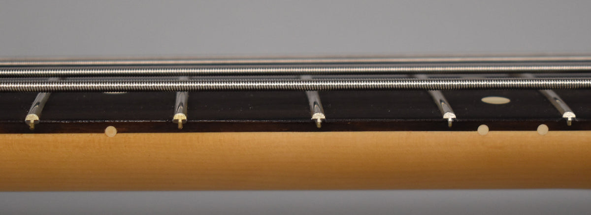 Close-up of the bass's dark fretboard with light fret markers and frets, showing four strings over a light maple neck.