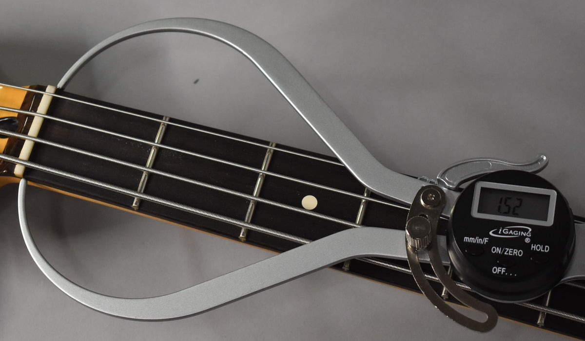 Close-up of the bass fretboard with a digital caliper measuring the fret height, displaying "1.52" on its screen.