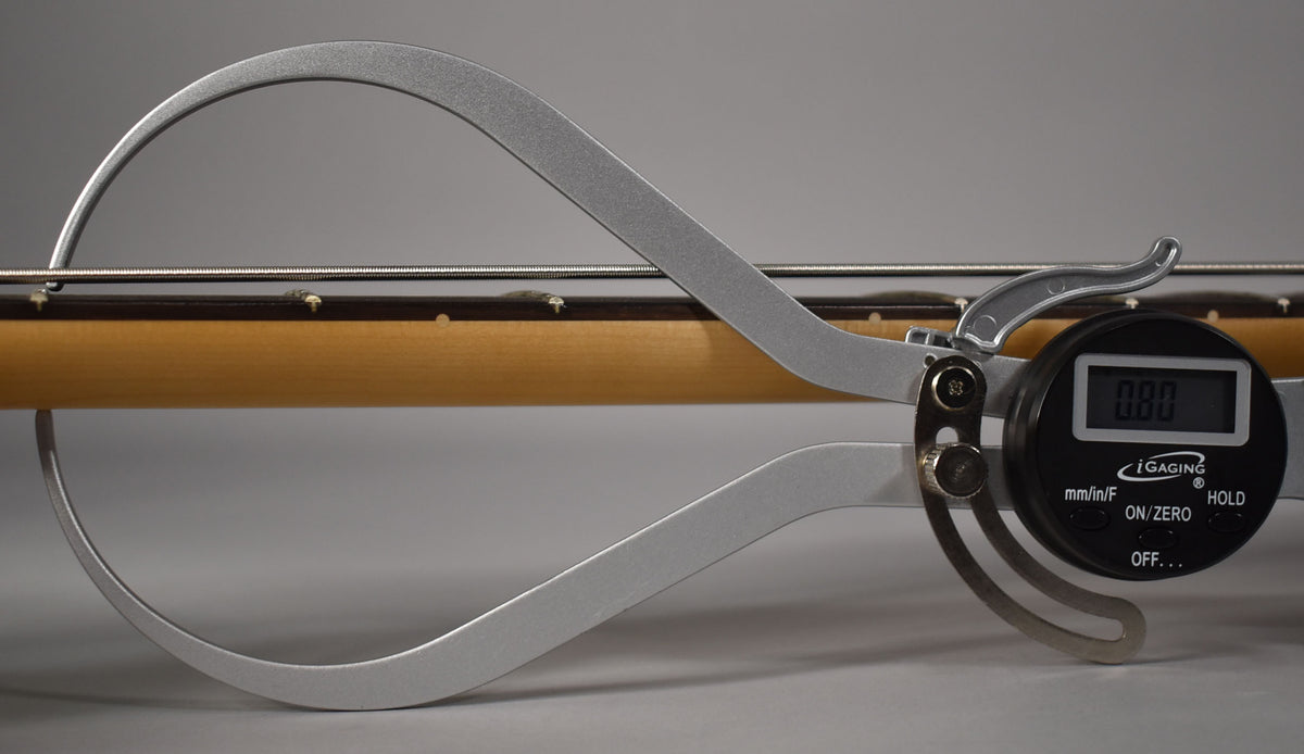 A digital caliper measures the neck relief of a guitar, displaying "0.80" on its screen.