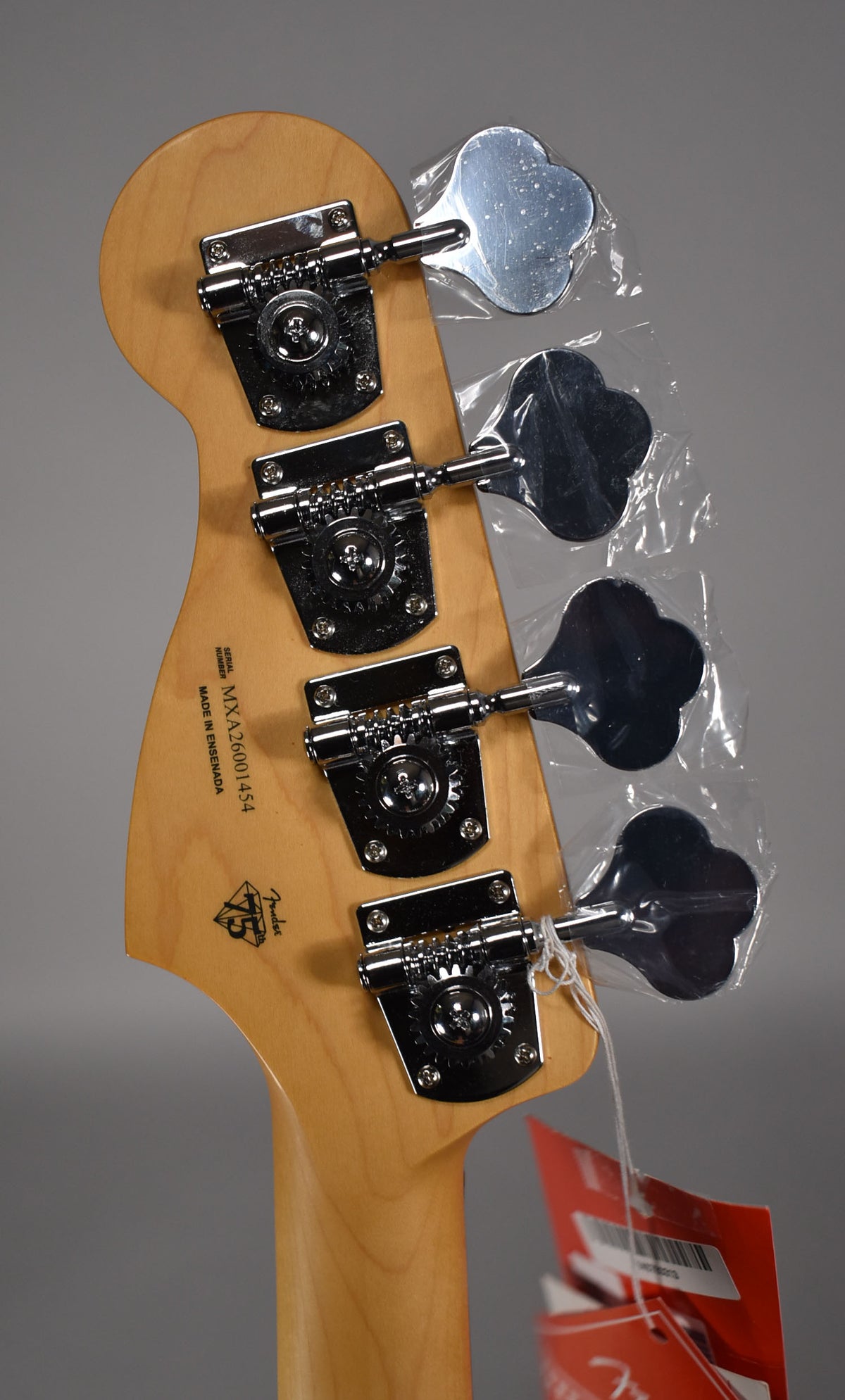 Rear view of the bass headstock and top of the neck, showing four chrome clover-leaf tuners, three still in plastic bags.