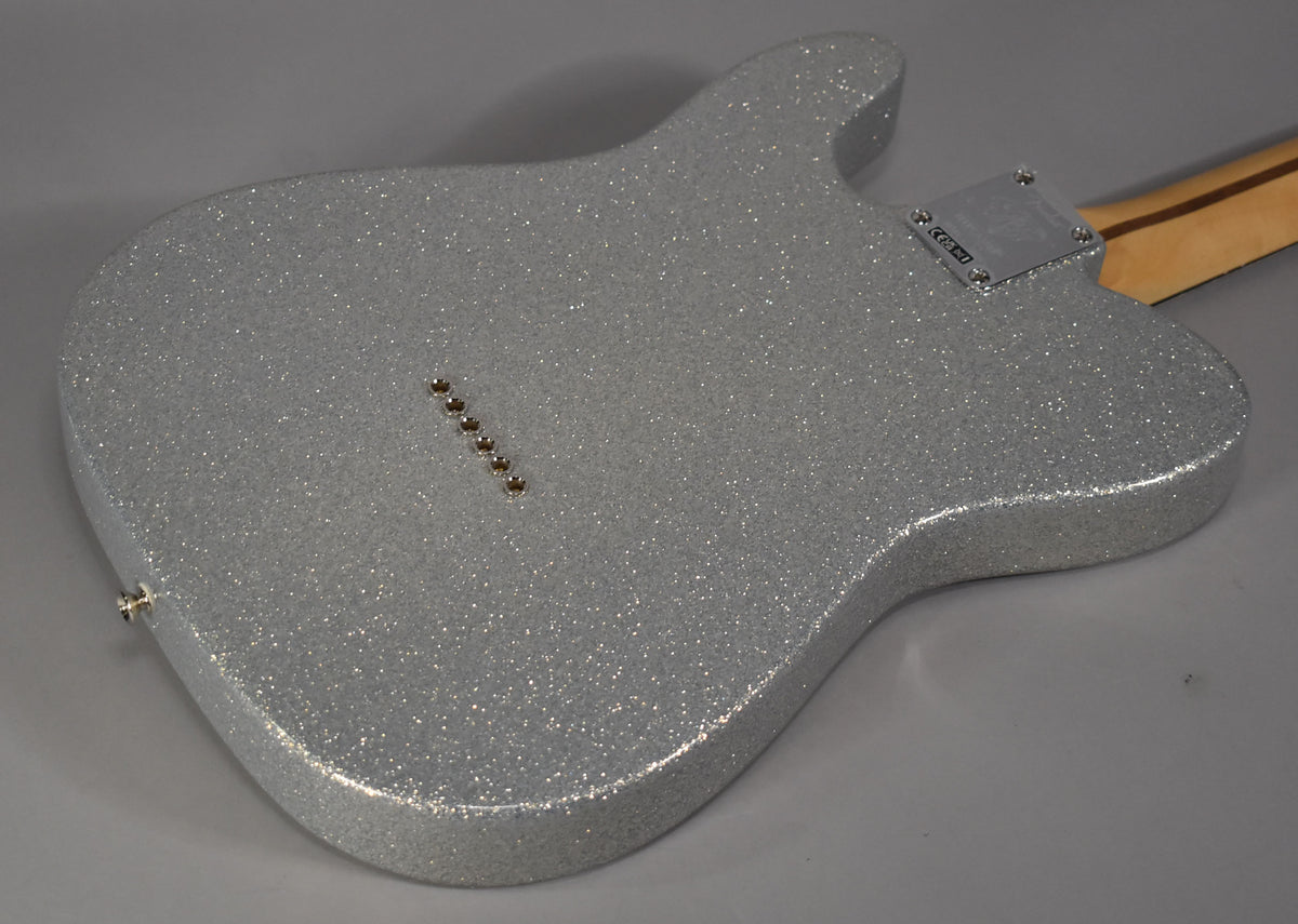 The back of a silver sparkle Telecaster body, angled from the lower left, with a chrome neck plate and six string ferrules visible.