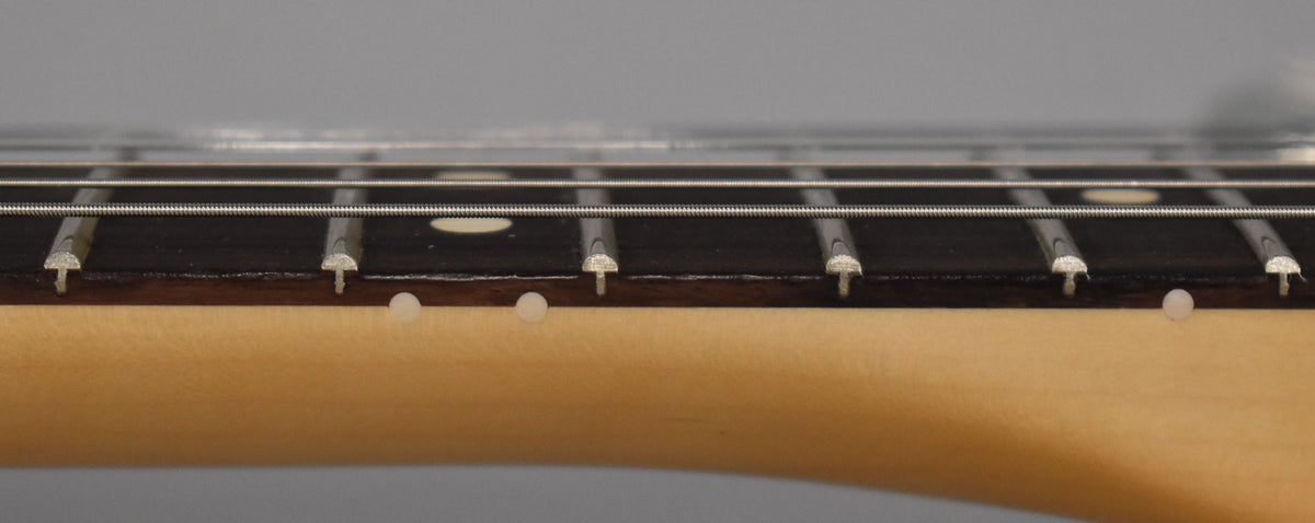 Close-up of the guitar's dark fretboard with light fret markers and side dots, showing the frets and strings from a low angle.