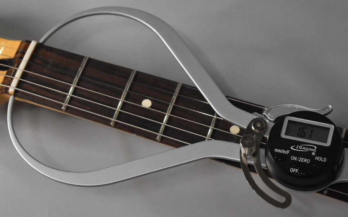 A digital fret height gauge measures the dark rosewood fretboard with light dot inlays and shiny frets.