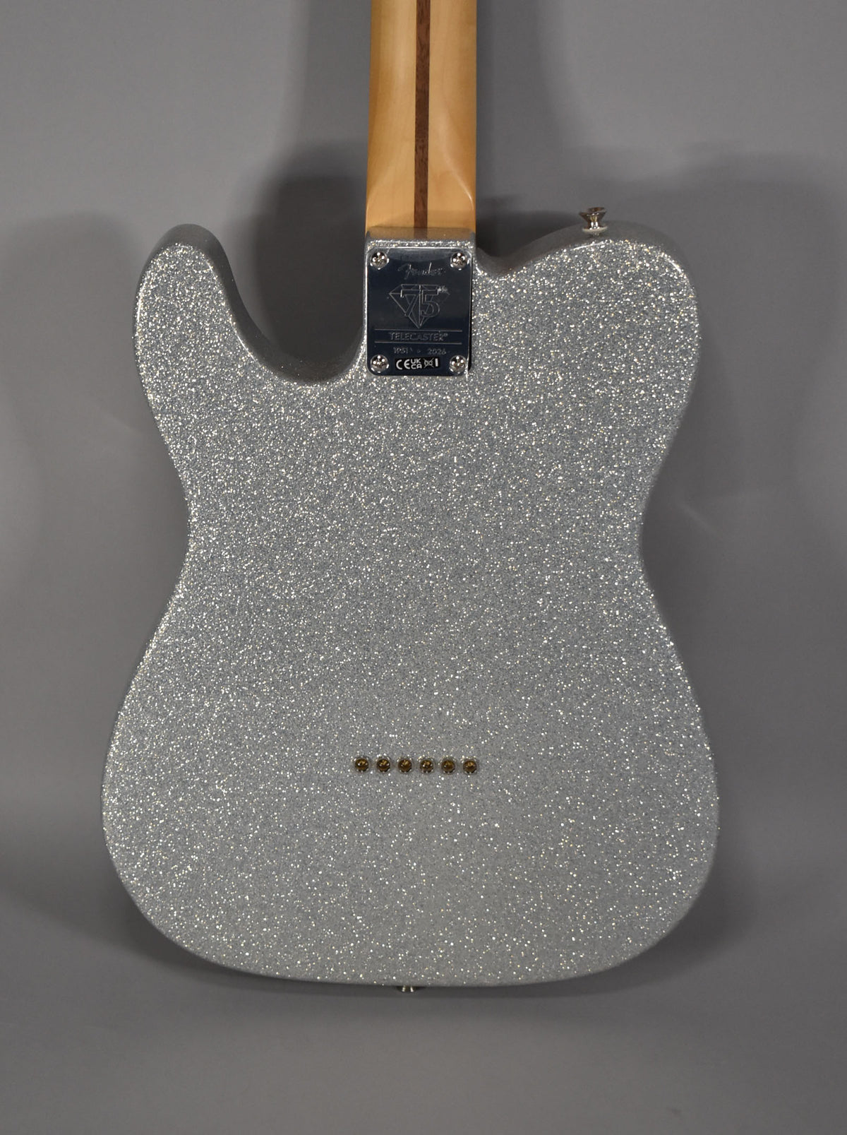 The back of a silver sparkle Telecaster body with a natural wood neck and six gold string ferrules.