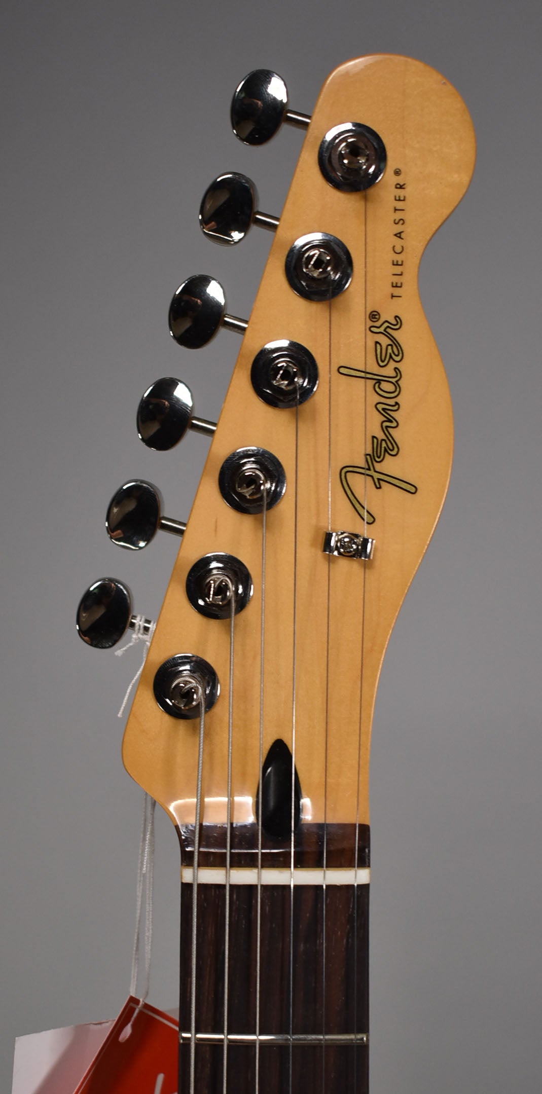 Close-up of the guitar's headstock, angled left, showing six chrome tuners, a string tree, and the dark rosewood fretboard.