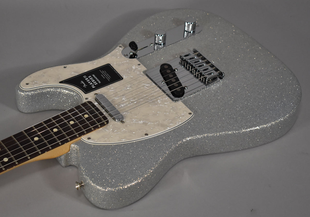 Angled view of a silver sparkle Telecaster body with a pearloid pickguard, chrome hardware, and a dark fretboard.