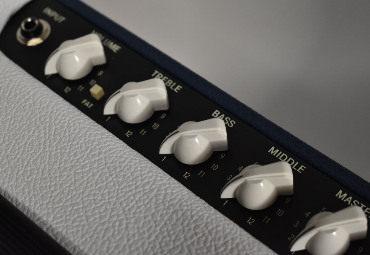 Close-up of the amp's black control panel with white chicken-head knobs, a yellow "FAT" button, and a white textured tolex finish.