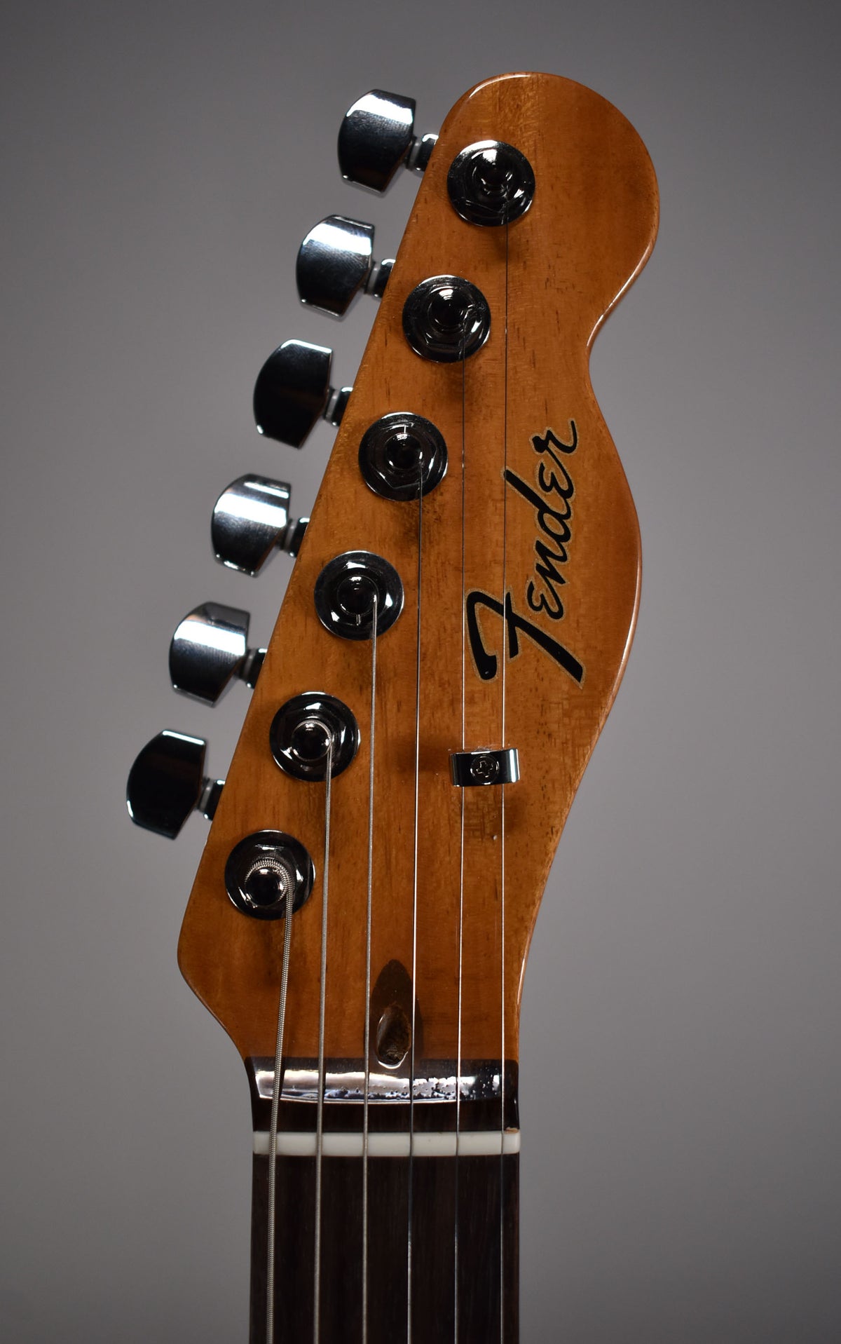 Close-up of the headstock, angled left, showing six chrome tuners, a string tree, and a dark rosewood fretboard.