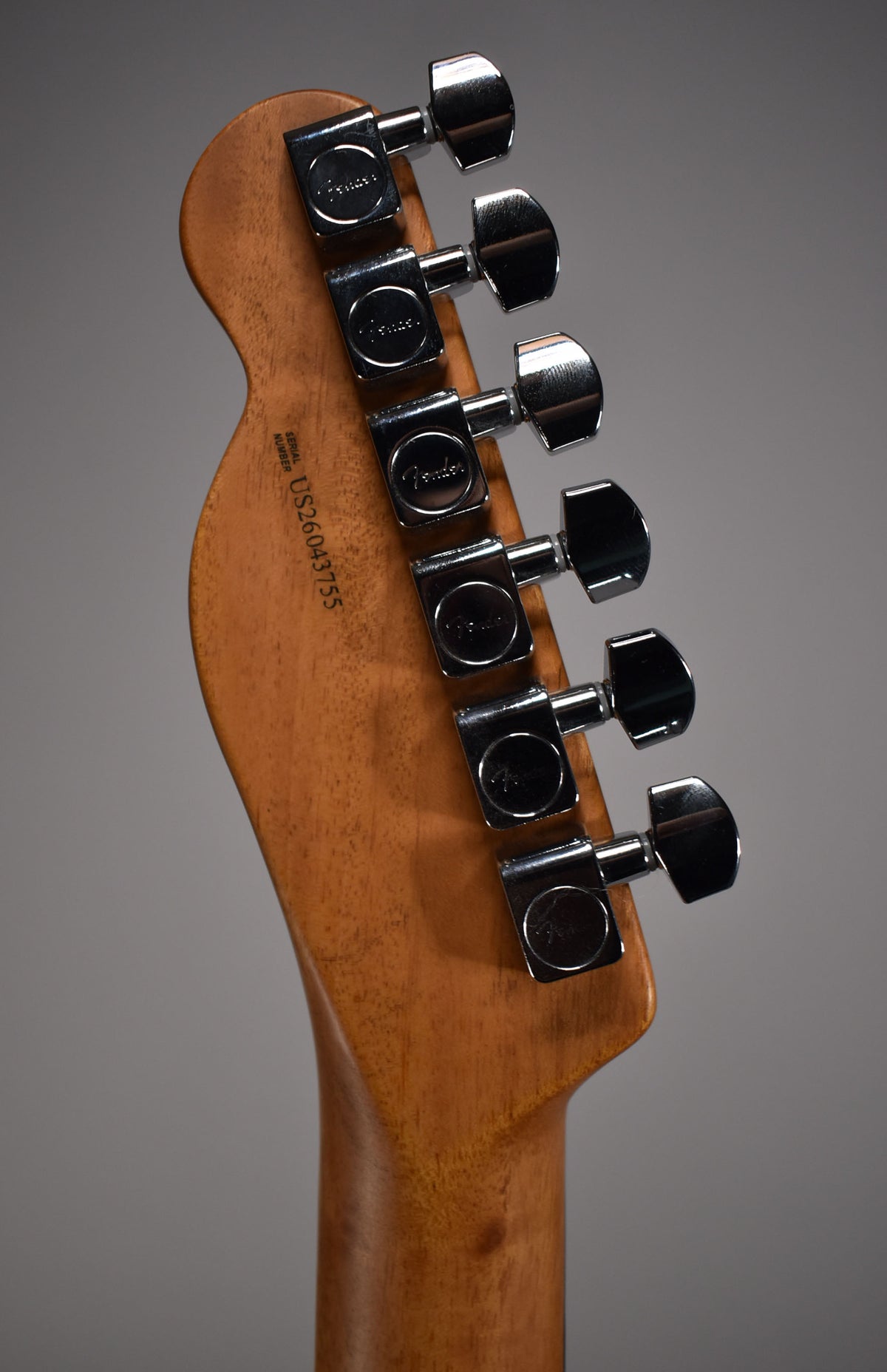 Close-up of the guitar's headstock and neck from behind, showing six chrome tuners and the serial number on the natural wood.