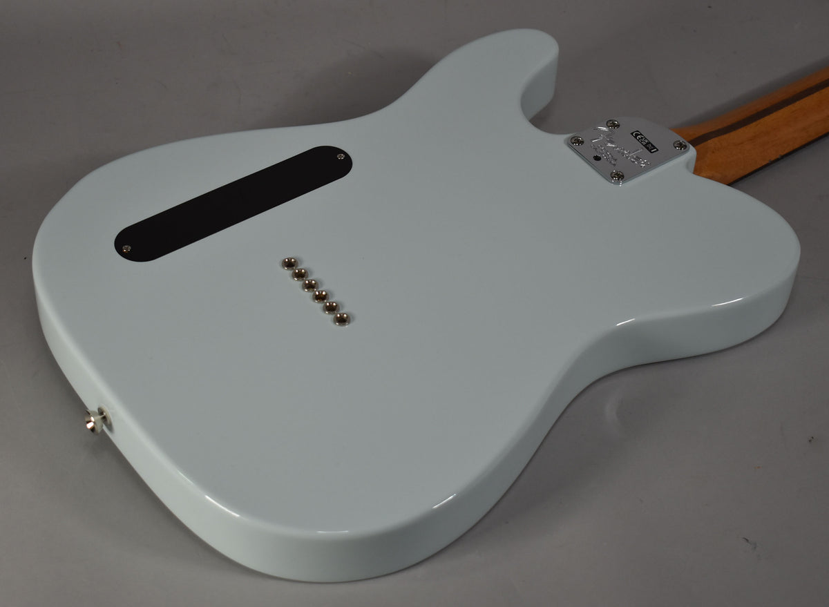 The back of a light blue solid body electric guitar, angled to show the neck plate, string ferrules, and control cavity cover.