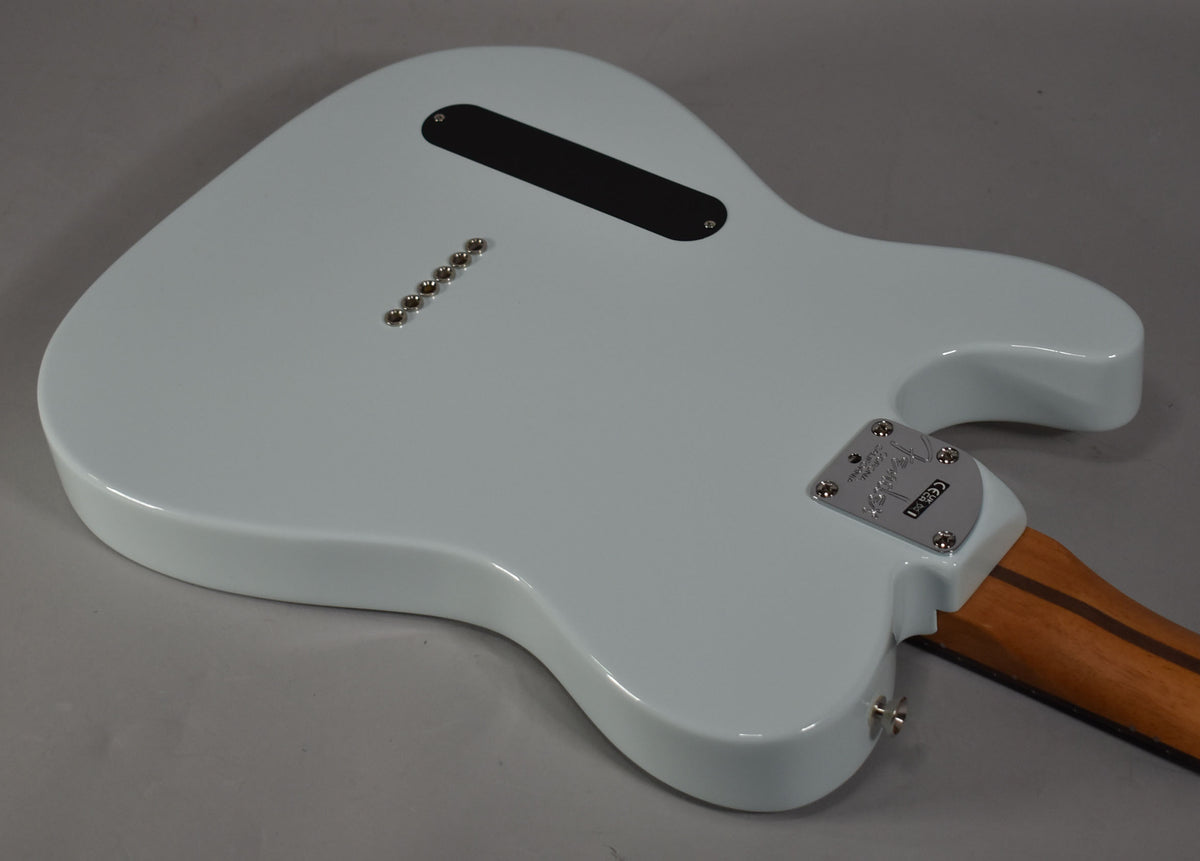 The back of a light blue Telecaster body, angled from the lower right, showing string-through ferrules and a black control cavity cover.