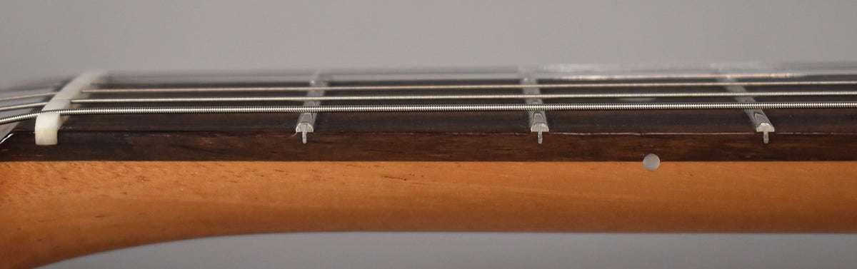 Close-up of the guitar's dark rosewood fretboard and light maple neck, showing the nut, frets, and strings from a low angle.