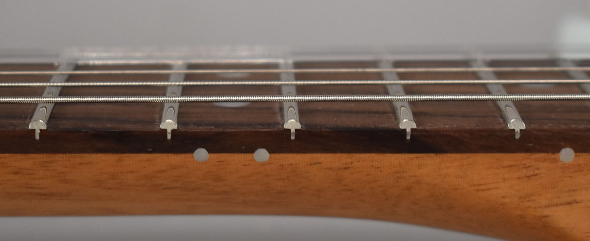 Close-up of the dark rosewood fretboard and light maple neck, showing five frets, strings, and three side dot markers.