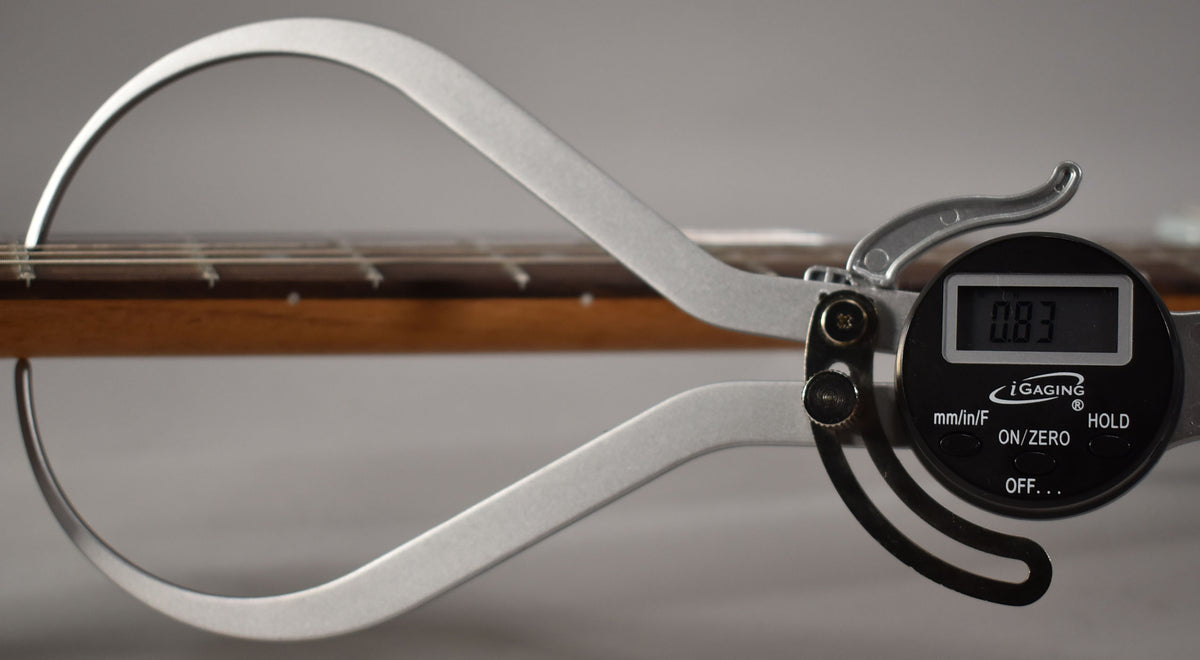 A digital caliper measures the guitar's fretboard, showing a reading of 0.83, with the instrument's neck visible.