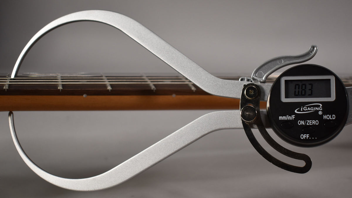 A digital caliper measures the guitar's fretboard and strings, showing a reading of 0.83 on its black display.