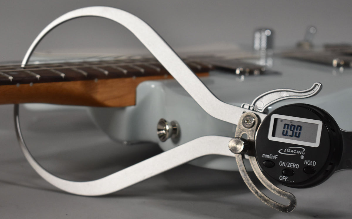 A digital caliper measures the fretboard radius of the light blue guitar, showing 0.90 on its screen.