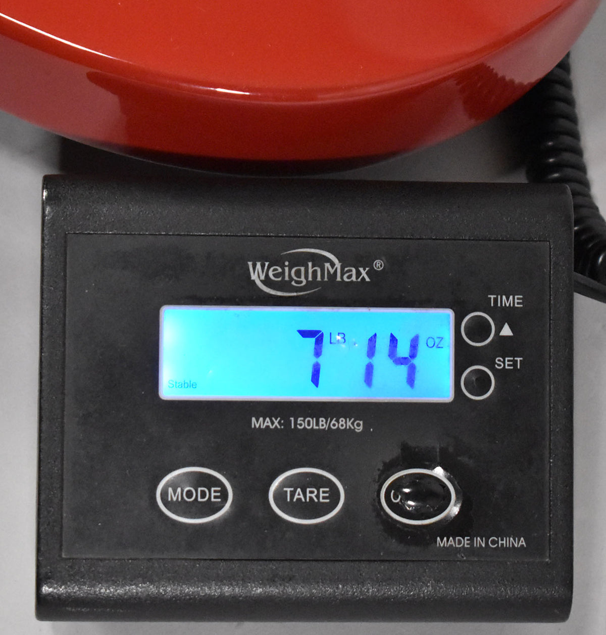 The guitar's red body rests on a black digital scale displaying "7 LB 14 OZ" in blue, with "Stable" and "Made in China" visible.