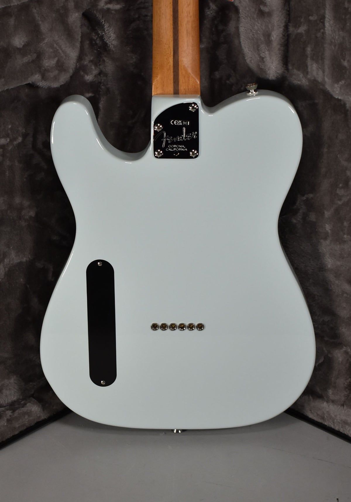 The back of a light blue Telecaster body with a black neck plate, string-through ferrules, and a dark control cavity cover.