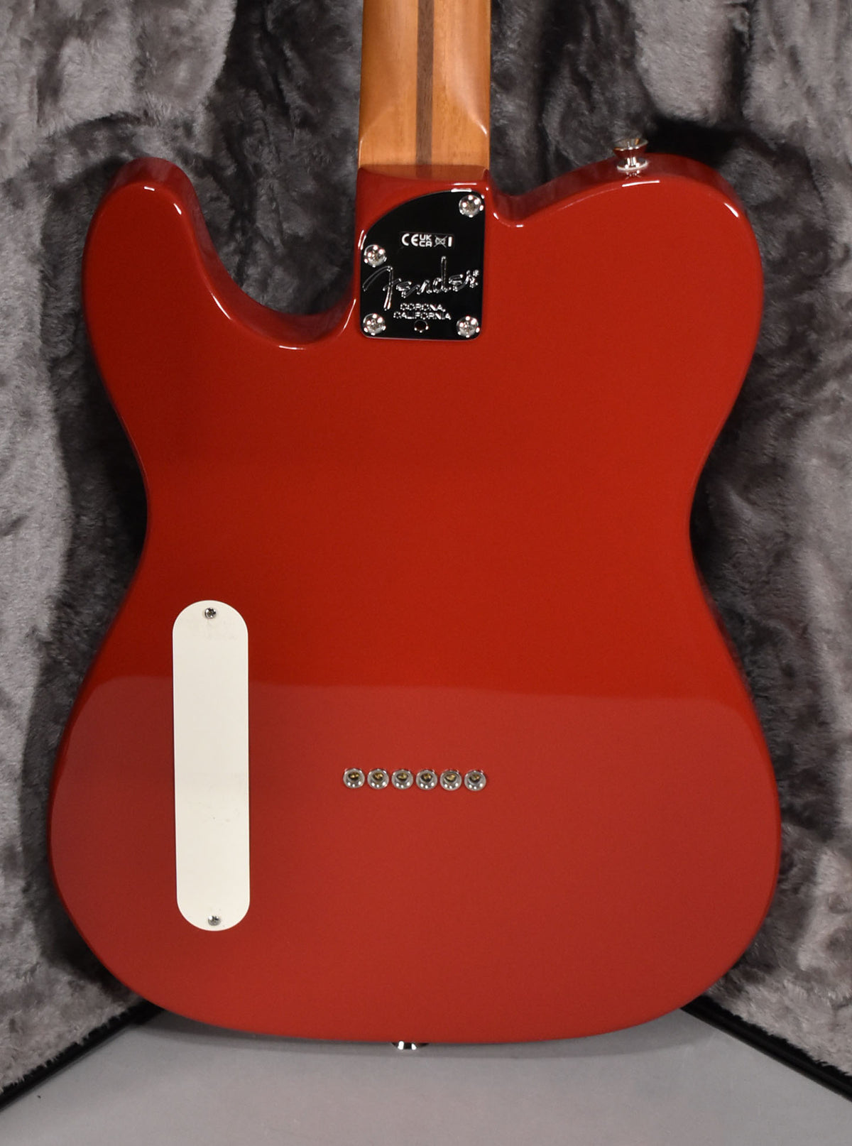 The back of a glossy red Telecaster, showing the neck plate, string-through-body ferrules, and a white control cavity cover.