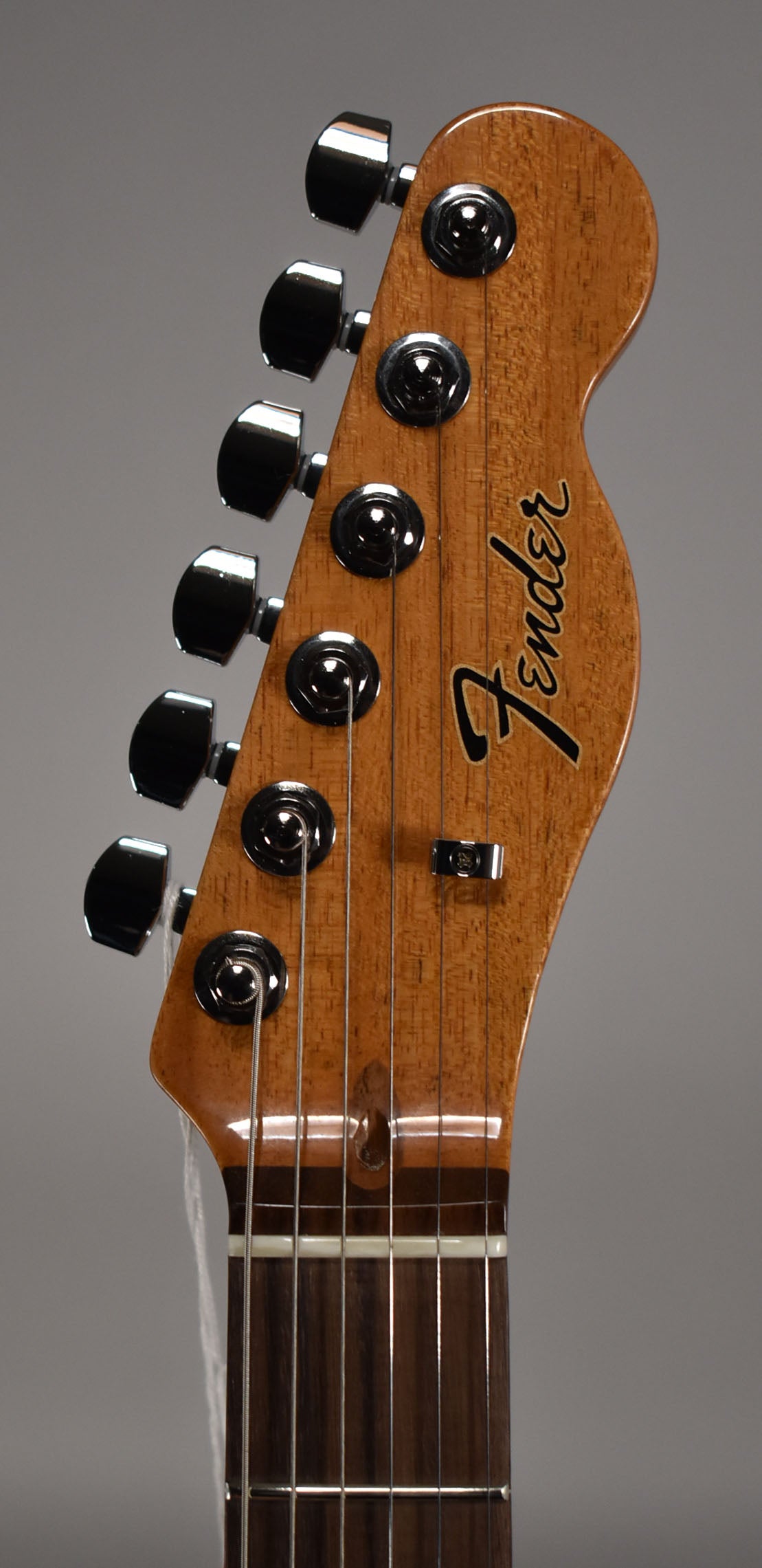Close-up of the guitar's headstock and upper fretboard, showing a natural wood finish, chrome tuners, and a string tree.
