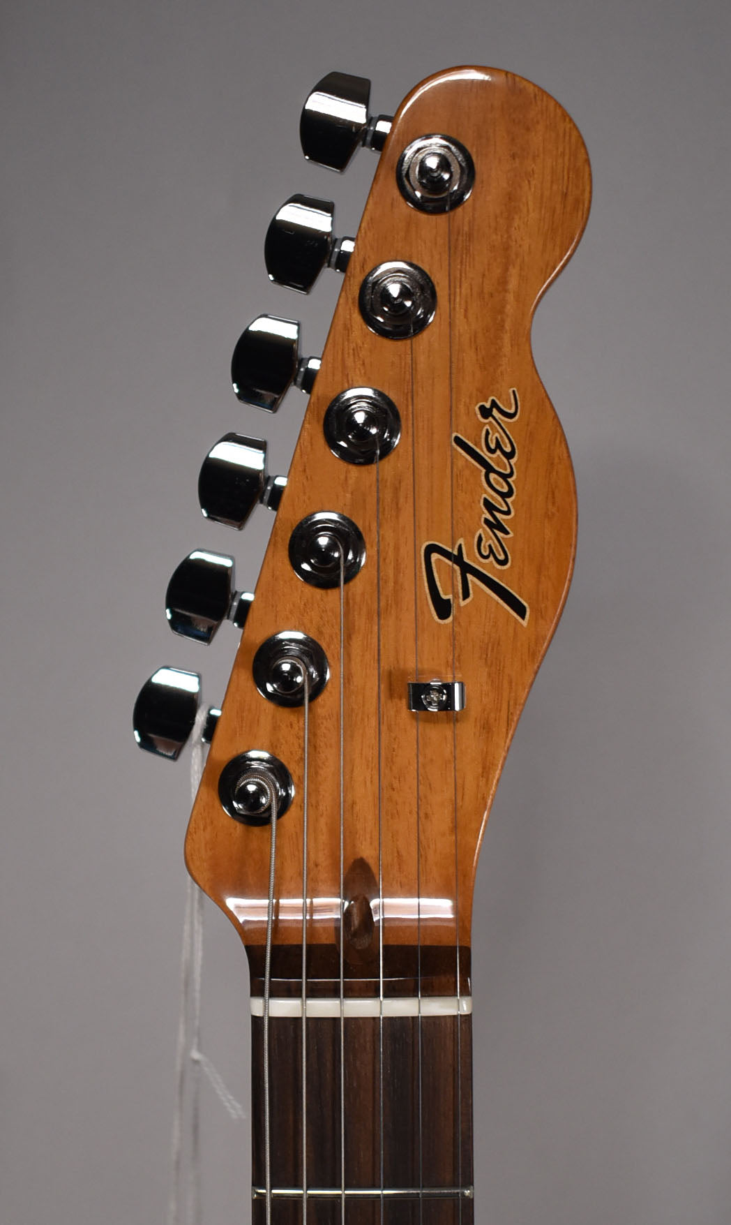 Close-up of the guitar's headstock, showing a natural wood finish, six chrome tuners, and a dark rosewood fretboard.