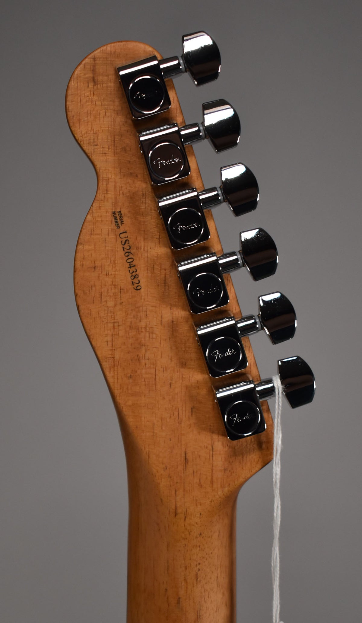 The back of a light brown wooden headstock with six chrome tuners, angled from the bottom left to the top right.