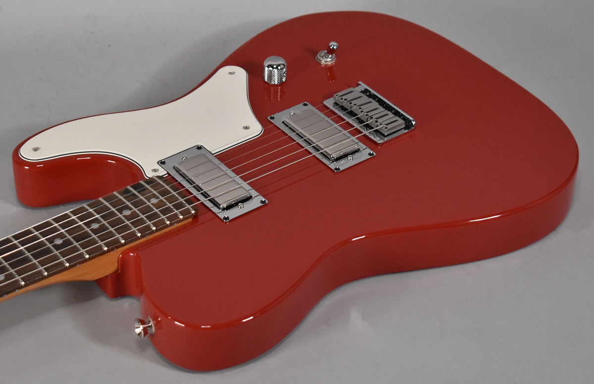 The glossy red guitar body, with a white pickguard, two chrome humbuckers, and a single chrome knob, is angled from the left.