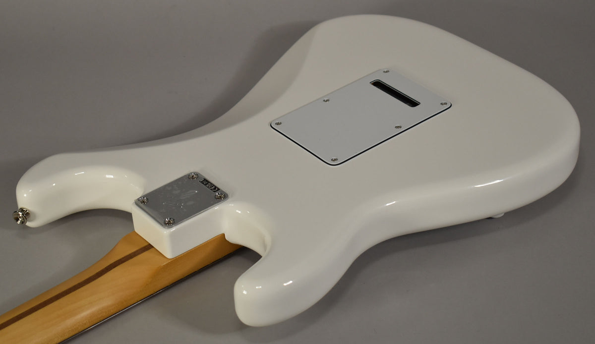 The guitar's glossy white back is angled, revealing a light maple neck, chrome neck plate, and a white tremolo cavity cover.