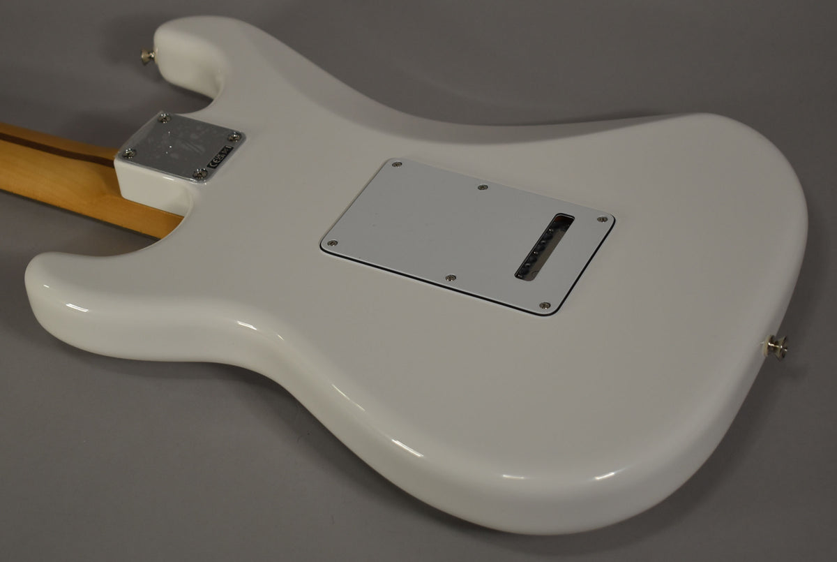 The guitar's glossy polar white back is angled from the neck joint to the lower bout, showing a chrome neck plate and tremolo cover.