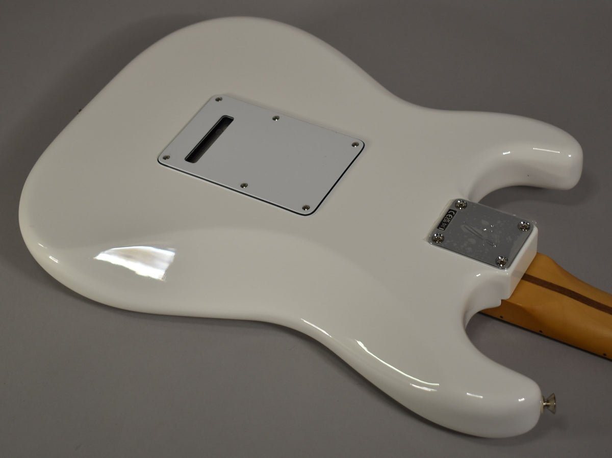 The back of a glossy polar white Stratocaster body, showing the tremolo cavity cover, neck plate, and a portion of the maple neck.