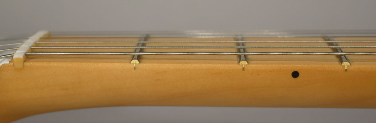 Close-up of the maple fretboard from the side, showing the white nut, four frets, strings, and a black dot inlay.