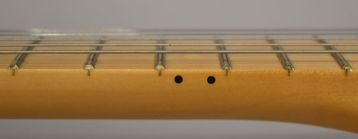 Close-up of the maple fretboard and frets from the side, showing two black dot inlays between the 7th and 9th frets.