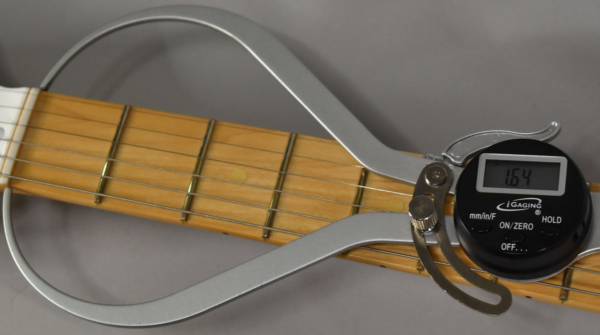 Close-up of the maple fretboard with a digital string action gauge showing "1.64" between the strings and frets.